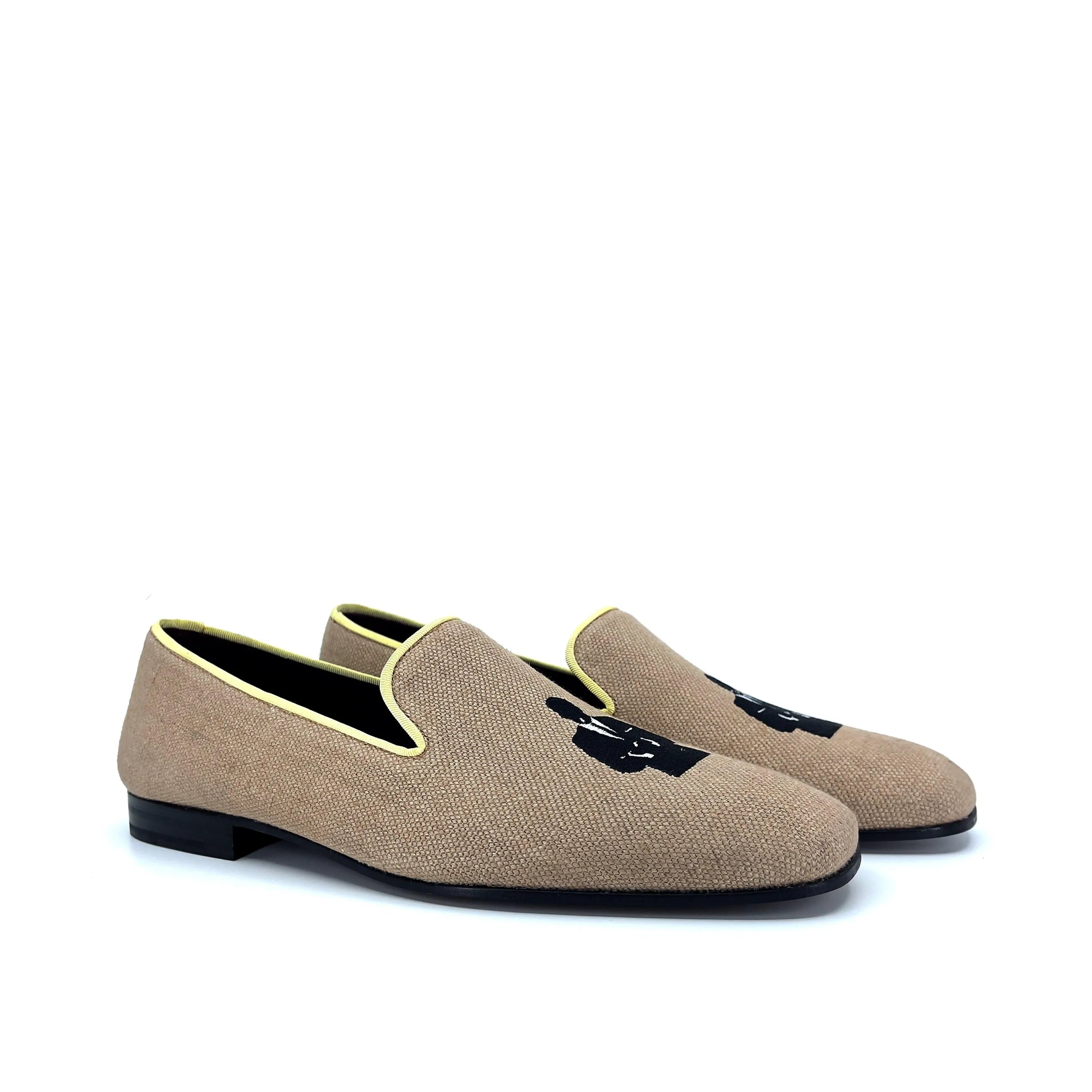 Beige canvas slip-on loafers with black embroidered silhouette design and contrasting yellow piping.