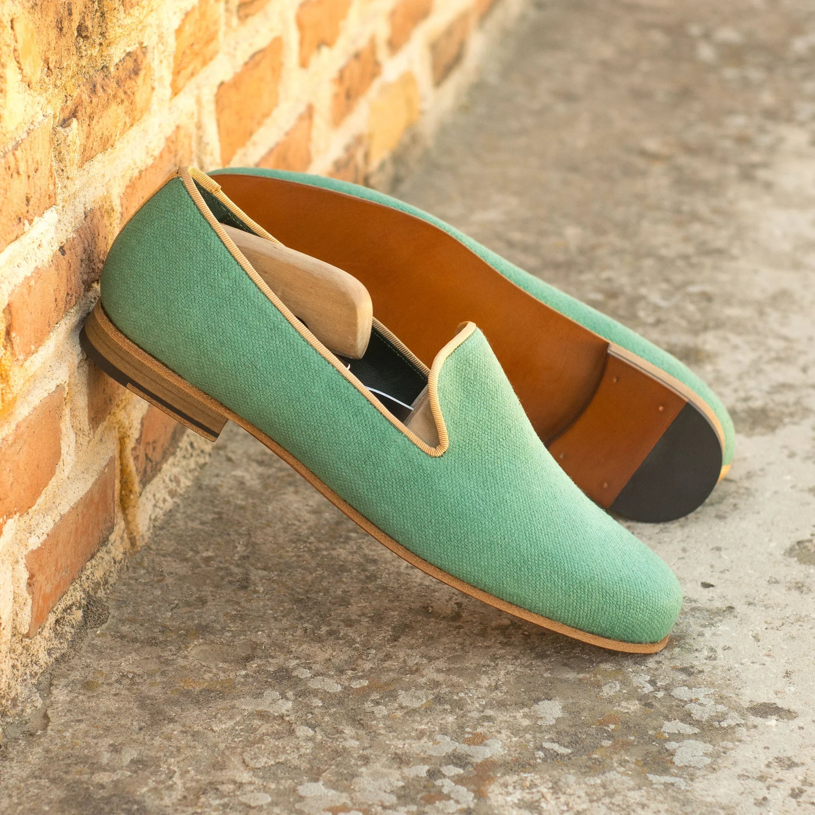 Mint green canvas slip-on loafers with tan leather trim and a contrasting brown interior lining.