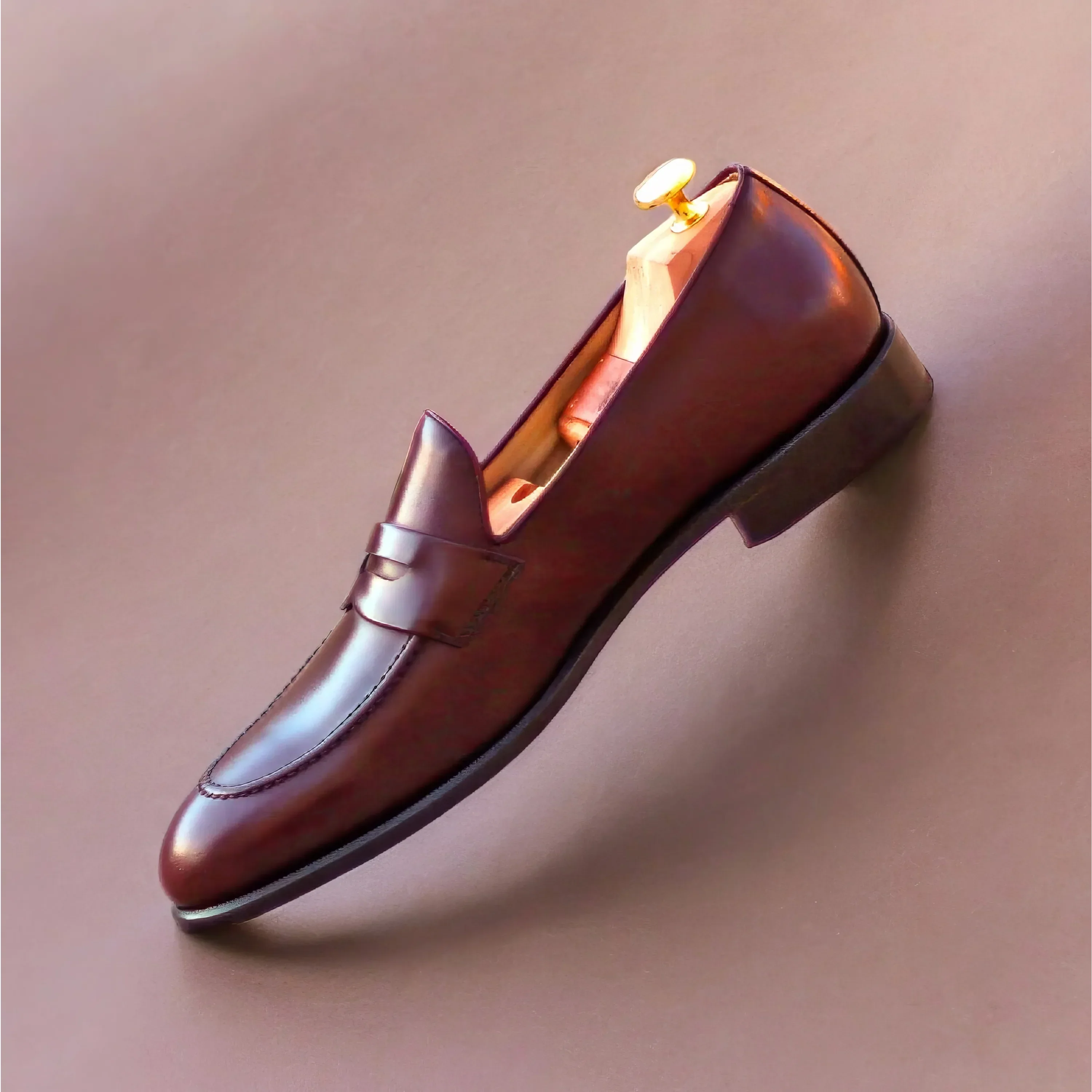 A polished brown leather loafer with a sleek, minimalist design and a gold-toned wooden shoe tree inside.