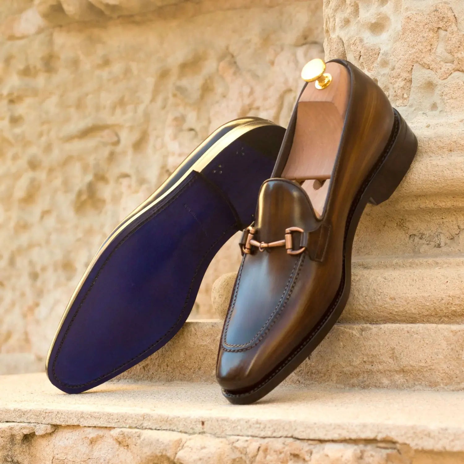 Brown leather horsebit loafer with navy blue toe cap and gold hardware.